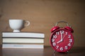 Alarm clock at 8am and stack of books with cup of coffee on wood