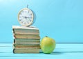 Alarm clock on stack of old books, apple on a blue background. School concept, education Royalty Free Stock Photo