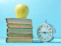 Alarm clock, stack old books, apple on a blue background. School concept, education Royalty Free Stock Photo