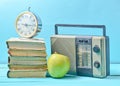 Alarm clock on stack of old books, radio receiver, apple on a blue background. Retro still life. Royalty Free Stock Photo