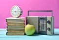 Alarm clock on stack of old books, radio receiver, apple on a pink background. Retro still life. Royalty Free Stock Photo