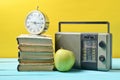 Alarm clock on stack of old books, radio receiver, apple on a yellow background. Retro still life. Royalty Free Stock Photo