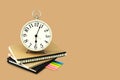 Alarm clock stacked on brown and black notebook with a post it note paper. Isolated on brown background with copy space and clip. Royalty Free Stock Photo