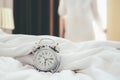 Alarm clock standing on bedside table has already rung early morning to wake up woman is stretching in bed in