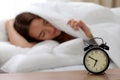 Alarm clock standing on bedside table has already rung early morning to wake up woman in bed sleeping in background Royalty Free Stock Photo