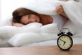 Alarm clock standing on bedside table has already rung early morning to wake up woman in bed sleeping in background Royalty Free Stock Photo