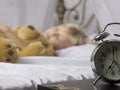 Alarm clock standing on bedside table. Wake up of an asleep young girl stopping alarm clock on a bed in the morning