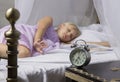 Alarm clock standing on bedside table. Wake up of an asleep young girl stopping alarm clock on a bed in the morning