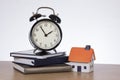 Alarm clock standing on books by model of house Royalty Free Stock Photo