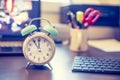 Alarm clock is standing on a grey desk, office stuff in the blurry background Royalty Free Stock Photo