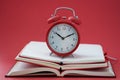 Alarm clock standing on pile of books on red background closeup Royalty Free Stock Photo