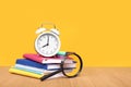 Alarm clock, stationery and a magnifier on the table, on a yellow background.