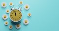 Alarm clock surrounded by flowers. Transitional change of summer time, daylight saving Royalty Free Stock Photo