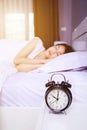 Alarm clock on table and woman sleeping on bed in bedroom Royalty Free Stock Photo