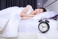 Alarm clock on table and woman sleeping on bed in bedroom Royalty Free Stock Photo