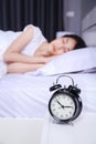 Alarm clock on table and woman sleeping on bed in bedroom Royalty Free Stock Photo