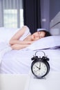 Alarm clock on table and woman sleeping on bed in bedroom Royalty Free Stock Photo