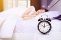 Alarm clock on table and woman sleeping on bed in bedroom Royalty Free Stock Photo