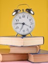 Alarm clock on top of piles of books on yellow background. Royalty Free Stock Photo