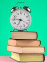 Alarm clock on top of piles of books on yellow background.