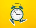 Alarm clock in toy sneakers walks on yellow background. Minimal time movement concept