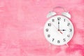 Alarm clock with twin bells and ringer showing 3 o'clock on pink background