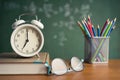 Alarm clock white and Colorful pencil, Book, Glasses on wooden table on blackboard background in classroom. Back to school concept