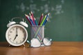 Alarm clock white and Colorful pencil, Glasses place on wooden table on blackboard background in classroom. Back to school concept Royalty Free Stock Photo
