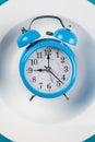 Alarm clock on the white plate on blue table. Time to eat, Breakfast, Lunch Time and Dinner concept Royalty Free Stock Photo