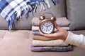 Alarm clock in women's hands on the Stack of cozy knitted sweaters background of the sofa. Warm clothes time concept Royalty Free Stock Photo