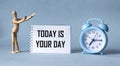 Alarm clock, wooden doll and notebook with the word Today is Your Day on a blue background Royalty Free Stock Photo