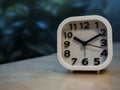 Alarm clock on wooden table with outdoor blur background.