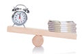 Alarmclock and stacked dollar bundles balancing on seesaw Royalty Free Stock Photo