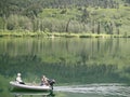 Couple fishing from small inflatable on calm water surrounded by wilderness