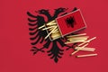 Albania flag is shown on an open matchbox, from which several matches fall and lies on a large flag