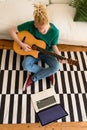 Albino african american man in the living room playing guitar and using laptop