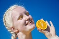 An albino young woman in a yellow blouse against a blue sky. holding slices of sliced orange. Royalty Free Stock Photo