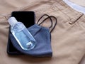 Alcohol bottle gel and blue fabric face mask with smartphone on brown long pants.