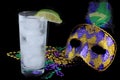 Alcoholic beverage and pourple, green and gold Mardi Gras beads with mask on a black bckground for a festive February holoiday ima