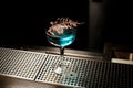 Alcoholic blue transparent cocktail in the glass decorated with a golden dry branch