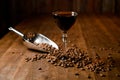 Alcoholic brown cocktail in the glass standing on the wooden table with coffee beans and metal scoop Royalty Free Stock Photo