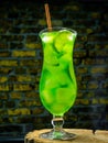 Alcoholic cocktail in a glass on a brick wall background. Vertical picture Green lemonade with ice. Summer fresh drink Royalty Free Stock Photo