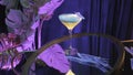 Alcoholic cocktail in a martini glass on purple background. Stock footage. Beautiful beverage on a glass table with soft Royalty Free Stock Photo