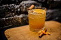 Alcoholic cocktail of orange color decorated with a slice of dried orange and a cinnamon stick