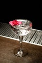 Alcoholic transparent cocktail with ice in the glass decorated with a pink rose bud