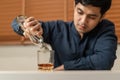 Alcoholism, depressed asian young man pouring, holding bottle whiskey into the glass, drinking alcohol beverage at night.