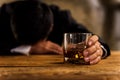 Alcoholism, depressed asian young man sleep on table while drinking alcoholic beverage, holding glass of whiskey alone at night.