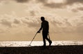 Man in silhouette using a metal detector on Aldeburgh beach. UK