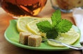Green saucer with slices of lemon, mint leaves, sugar cubes. Mug of herbal tea.