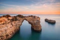 Algarve beach, romantic couple watching the sunset. Loving moment under natural arch carved in stone is a tourist attraction of th Royalty Free Stock Photo